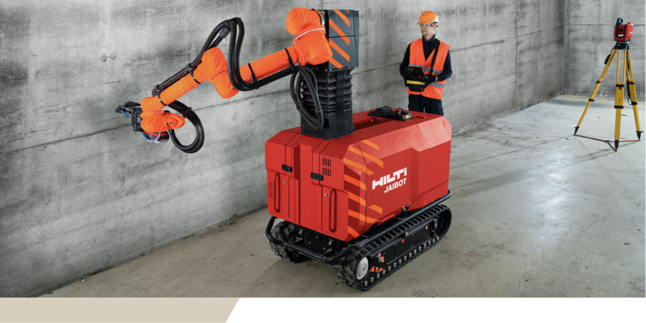 Ein Bauarbeiter in einer Warnweste bedient einen Hilti Jaibot, der an der Wand arbeitet.