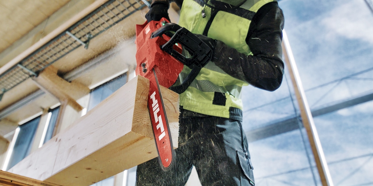 Arbeider met Hilti SCN 60-22 accu kettingzaag zaagt een houten balk