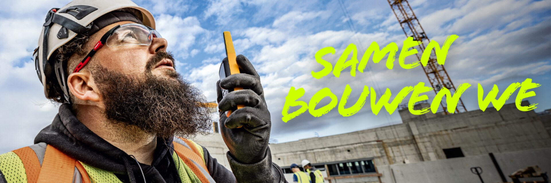 Een man spreken in bouwkleding over een project , op de achtergrond is de bouwplaats zichtbaar.