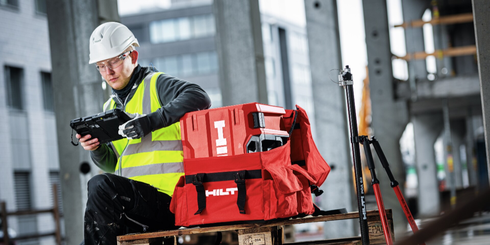 Een persoon in werkkleding voor een Hilti-koffer kijkt op een tablet.